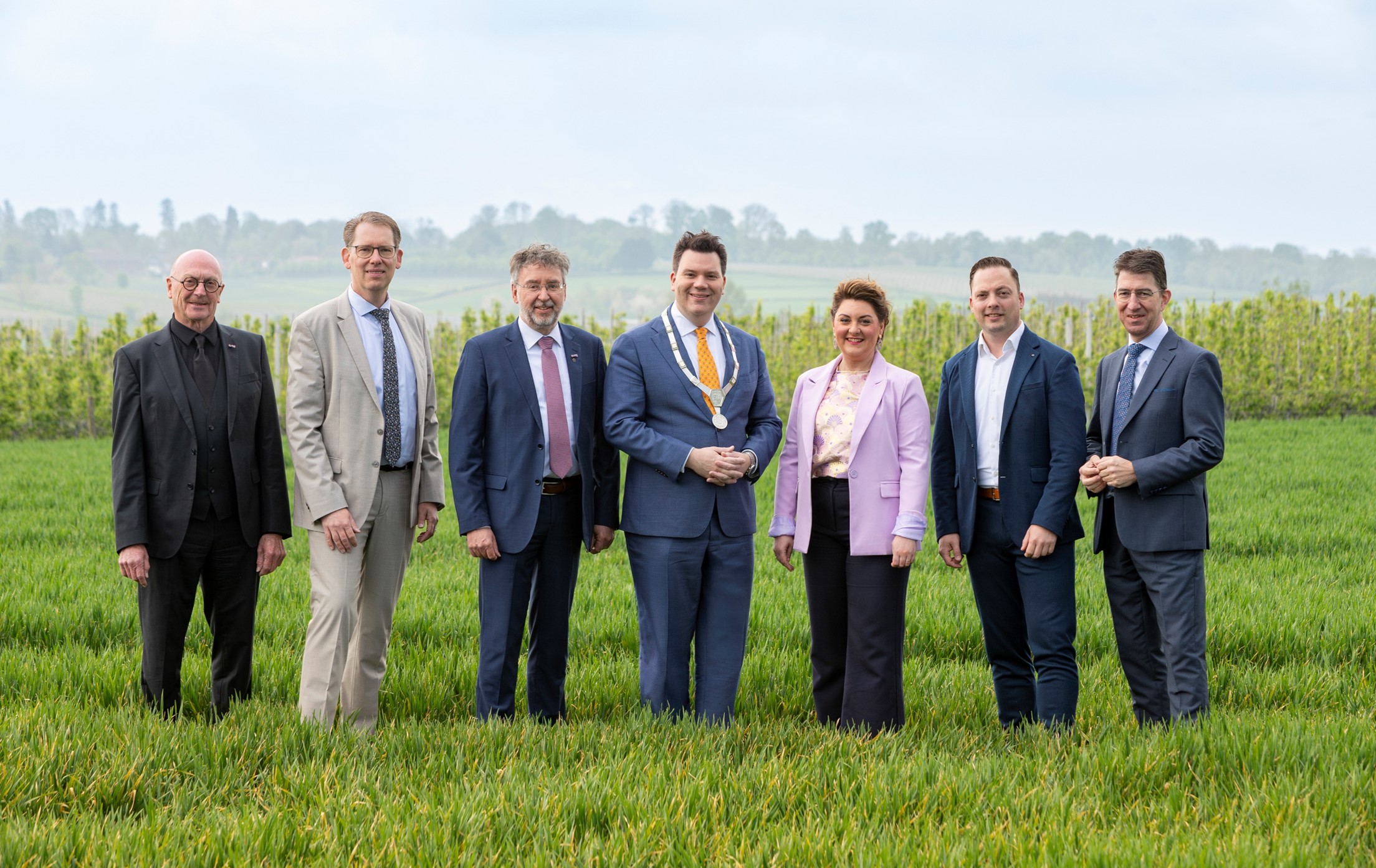 Burgemeester en wethouders  lente 2025 staan in een weliland met op de achtergrond het heuvellandschap